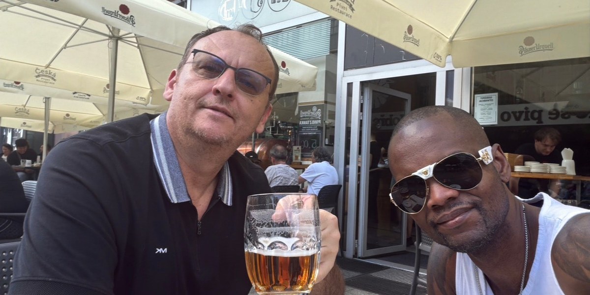 Zwei Freunde stoßen auf einer Café-Terrasse mit Bier an